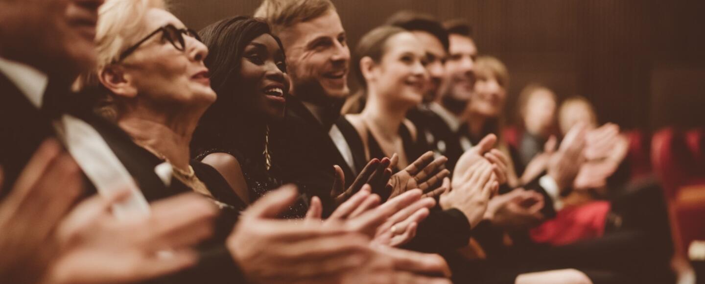 The audience in the front row of a concert smiles and applauds