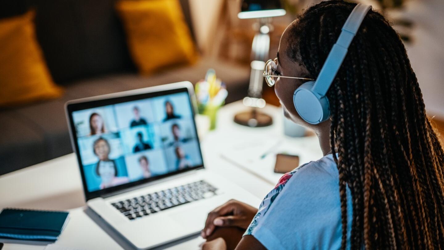 A woman in headphones looks at a Zoom call on her laptop