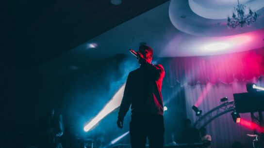 A singer performing on a dark stage in front of coloured lights